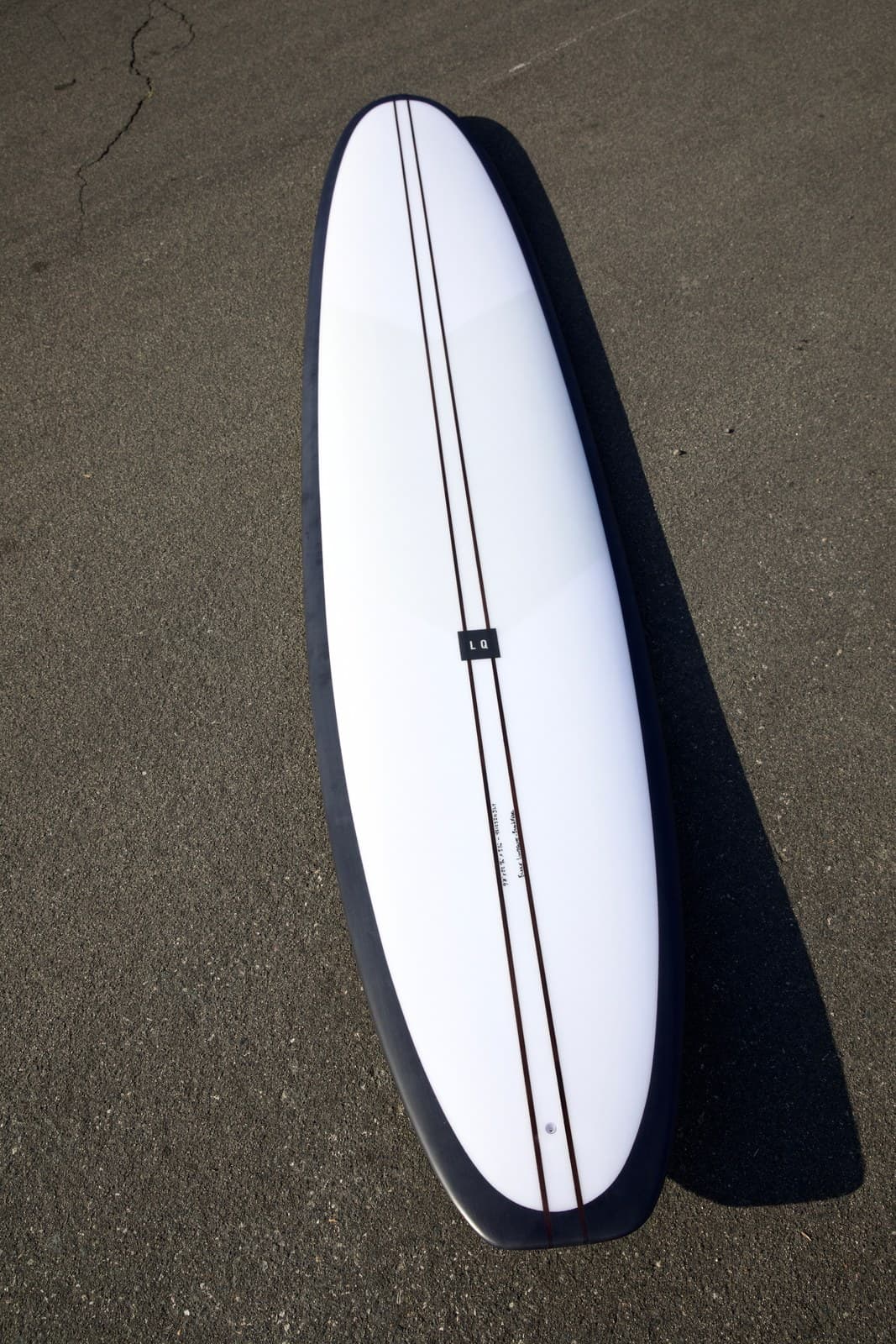 Black Pearl longboard white deck with black rails on asphalt lifestyle shot